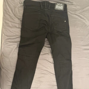 Svarta Replay Anbass jeans - Svarta Replay Anbass jeans med klassisk femficksdesign och snygga detaljer på bakfickorna. Jeansen har smal passform och är tillverkade i stretchigt bomullsmaterial för extra komfort. Perfekta för dig som gillar stilrena och moderna jeans. Använt ett par ganger bara pris 450 kan diskuteras vid snabb affär 