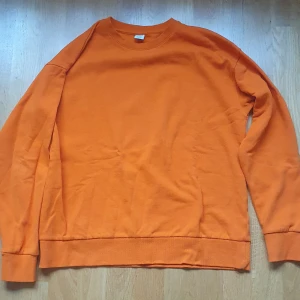 Orange sweatshirt från Lindex, strl 170 - En enkel och snygg orange sweatshirt från Lindex i barnstorlek 170. Tröjan har rund hals, långa ärmar och är tillverkad av återvunnen bomull. Perfekt för dig som gillar färg och vill ha en basic tröja med skön passform. Lite använda, bra skick.