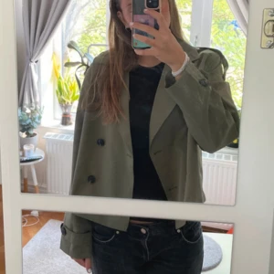 Olivgrön croppad trenchcoat JJXX - En superfin olivgrön trenchcoat som knappt är använd! Mycket bra skick och är en tunnare jacka som passar perfekt till våren/hösten. Köpt för 799.95 kr. Skriv för fler bilder!