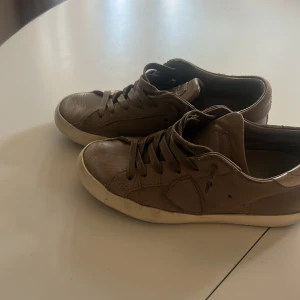 Philippe models  - Snygga bruna sneakers från Philippe Model med klassisk låg profil och rund tå. Skorna är i skinn med matchande bruna snören och vit sula. Perfekta för dig som gillar stilrena och bekväma skor med en exklusiv känsla.