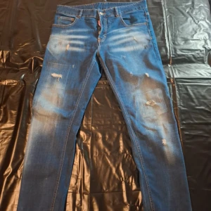 Blå Dsquared2 jeans med slitningar - Säljer ett par blå jeans från Dsquared2 med snygga slitningar och ljusa tvättade partier. Klassisk femficksmodell med raka ben och normal passform. Jeansen har coola detaljer och är tillverkade i bomullsdenim.