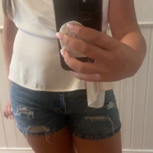 Blå jeansshorts från Lager 157 - Säljer ett par blå jeansshorts från Lager 157 med snygga slitningar och råa kanter i storlek S. Modellen lowwaist  är och har klassiska fem fickor samt knapp och dragkedja framtill. Perfekta för sommarens alla äventyr!