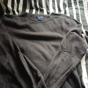 Mörkgrå stickad tröja Jack & Jones - Säljer en mörkgrå stickad tröja från Jack & Jones i storlek S. Tröjan har en rund halsringning och ett grovt, strukturerat stickat mönster som ger en cool och avslappnad vibe. Perfekt för kyligare dagar och enkel att matcha med jeans eller chinos.
