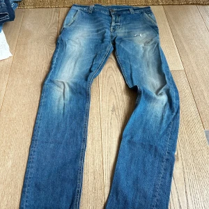 Dondup jeans - Säljer ett par klassiska blå jeans med snyggt slitna detaljer och raka ben. Jeansen är tillverkade i Italien och har en skön passform. Materialet är bomull med lite polyester i fickorna. Perfekta för dig som gillar en tidlös jeanslook. Dondup
