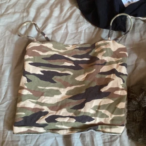 Camo linne från Gina Tricot XS - Säljer ett camouflagemönstrat linne från Gina Tricot i storlek XS. Linnet har tunna axelband och är gjort i mjuk bomullsmix. Färgerna går i grönt, beige och brunt för en klassisk army-look. Perfekt för dig som vill sticka ut med en edgy stil.