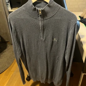 Grå stickad polotröja från Gant - Snygg blå stickad polotröja från Gant med half zip och diskret logga på bröstet. Tröjan har lång ärm och ribbad krage, perfekt för lager-på-lager-stil. Passar dig som gillar klassisk och stilren look. 
