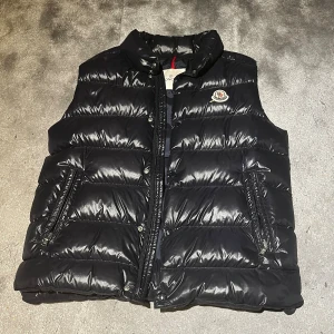 Svart dunväst Moncler - Snygg svart dunväst från Moncler, tröjan har tyvär hål i fickorna som syns på sista bilden men går nog enkelt att laga och generellt gör inte så mycket då hålet inte är så stort. Äkta såklart 