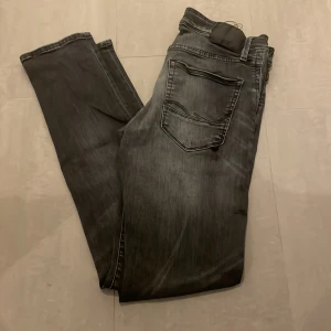 Slim fit svarta jeans Glenn 32/34 - Svarta slim fit jeans från Glenn i storlek 32/34. Jeansen har en snygg tvättad look med klassiska fem fickor och smal passform. Perfekta för dig som gillar en stilren och modern vibe. Materialet är jeans och färgen är mörkgråsvart.