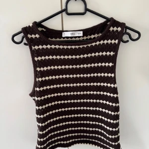 Brun och vit stickad linnetopp MNG - Säljer en stickad linnetopp från MNG i storlek S. Toppen har ett brunt och vitt randigt mönster med en cool struktur. Ärmlös modell med rund halsringning, perfekt för varma dagar eller lager på lager. Superfin till både jeans och kjol!