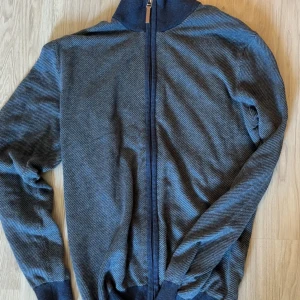Grå zipjacka i manchester - Snygg grå full zip med diskret mönster från Hansen & Jacob. Passar perfekt både till vardags eller till finare tillfällen. Skick 9,5/10. Tröjan var en present som aldrig kom till användning, därav är den endast använd någon enstaka gång. Tröjan säljs inte längre men liknande tröjor hos H&J säls för cirka 3000kr. Denna säljer jag för 299kr (priset är inte hugget i sten) Storlek M, passar även på dig som har S!