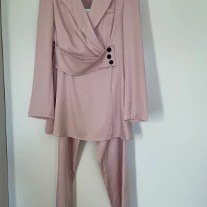 Rosa kostym set - Rosa kostym set i utmärkt skick. Har ett inbyggt bälte som syns på bild vilket ger en fin figursydd form. Inga skador eller fläckar, de har aldrig använts. 