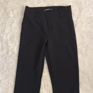 Svarta bootcut kostymbyxor Gina Tricot - Svarta kostymbyxor från Gina Tricot med bootcut-ben, mellan midja och snygga fickor med lock och knappar bak. Byxorna har bälteshällor och stängs med två knappar framtill. Perfekta för en clean och stilren look. Jeansen är oanvända!