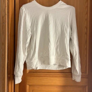 Vit tröja med pärlknappar Holly & Whyte - Säljer en vit långärmad tröja från Holly & Whyte by Lindex. Tröjan har puffiga axlar och snygga pärlknappar på ena axeln som detalj. Tillverkad i mjuk bomull och har en klassisk rund halsringning. Perfekt för dig som gillar stilrena plagg med en twist.