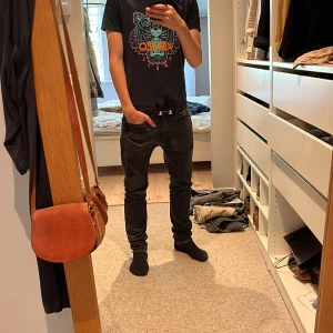 Svart Kenzo t-shirt med tigertryck - Svart t-shirt från Kenzo med ikoniskt tigertryck i neonfärger och orange Kenzo Paris-text på bröstet. Klassisk rund hals och korta ärmar. Skön passform och tillverkad i mjuk bomull. Perfekt statement-plagg för dig som gillar streetstyle.