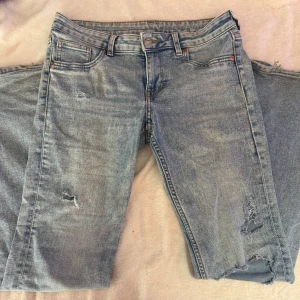 Ljusblå slitna jeans med bootcut - Säljer ett par ljusblå jeans med bootcut och snygga slitningar på båda benen. Jeansen har klassisk femficksdesign, knappgylf och är tillverkade i denim. Perfekta för dig som gillar en avslappnad och trendig look. Storlek 40 men mindre i storlek