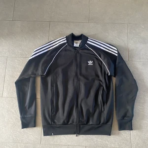 Svart Adidas track jacket med vita ränder - Svart addidas sst kofta i storlek L. Säljs för den längre går till användning och har inga problem alls