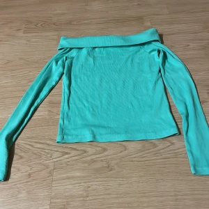 Turkos offshoulder topp - Snygg turkos offshoulder topp med långa ärmar och ribbad struktur. Perfekt för dig som vill ha en trendig och stilren look. Toppen har en bred kant upptill som ger en cool och modern känsla.