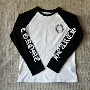 Chrome Hearts svartvit långärmad tröja - Säljer en svartvit långärmad tröja från Chrome Hearts med stora tryck på ärmarna och ryggen. Tröjan har kontrastfärgade ärmar och klassisk logga på bröstet. Tillverkad i mjuk bomull och har en avslappnad passform. Perfekt för dig som gillar streetwear. Skriv om ni har några funderingar på produkten eller priset 