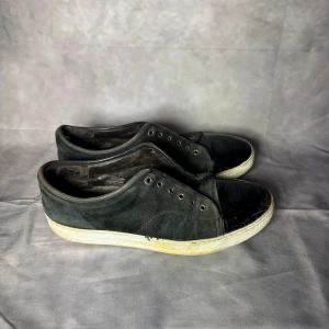 Lanvin sneakers - Svarta sneakers med ovandel i mocka och tåparti i blankt material. Skorna har vita sulor och klassisk snörning (utan skosnören). Perfekta för en avslappnad streetstil. Pris utifrån skick.