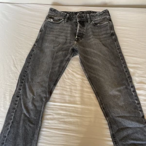 Grå loose fit jeans Jack & Jones - Säljer ett par grå loose fit jeans från Jack & Jones, modell Chris. Jeansen har klassisk femficksdesign, raka ben och snyggt tvättad finish. Perfekta för dig som gillar en avslappnad och trendig look. Materialet är mjukt denim i bomull. 29/30 i storlek.