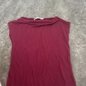Vinröd topp från 157 XS - Enkel vinröd topp från 157 i storlek XS. Modellen är ärmlös med bred halsringning och rak passform. Perfekt att styla med jeans eller kjol för en clean look. Tunt och mjukt material som känns skönt mot huden.