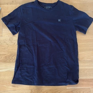 Svart t-shirt från Calvin Klein Jeans - Svart t-shirt från Calvin Klein Jeans med klassisk passform och rund hals. Liten CK-logga på bröstet.