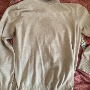 Beige polotröja från Saint Tropez - Säljer en beige polotröja från Saint Tropez i storlek L. Tröjan har ribbade muddar och hög krage, är långärmad och har en klassisk, stilren look. Perfekt för lager-på-lager och enkel att matcha med olika outfits.