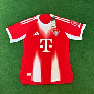FC Bayern München matchtröja Adidas 25/26 - Riktigt snygg FC Bayern München matchtröja från Adidas i rött och vitt med klubbmärke och sponsortryck. Tröjan har korta ärmar, vit krage och klassiska Adidas-ränder på axlarna. Tillverkad i lätt och ventilerande funktionsmaterial.