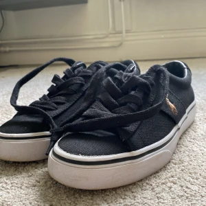Svarta sneakers från Polo Ralph Lauren - Svarta sneakers från Polo Ralph Lauren med klassisk låg profil, vit sula och svart snörning. Skorna är i canvasmaterial och har den ikoniska broderade Polo-loggan på sidan. Perfekta för en clean och stilren look. Helt oanvända!