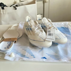 Adidas F50 Elite FG Polar Victory - vit/silver/blå - Adidas F50 Elite FG fotbollsskor, storlek 39, i vitt med blåa samt silvriga detaljer och de tre klassiska ränderna på sidan. Lätta och sköna fotbollsskor med snörning, platt sula med dobbar och syntetmaterial. Kommer med extra innersulor och en snygg vit/blå påse med F50-tryck. Bevis på att de är Elite finns på sista bilden och de är använda ett fåtal gånger. ⚽️😇Nypriset var 2600kr när de köptes under rea. Tveka inte på att fråga om fler bilder eller något annat ni undrar över. 💘