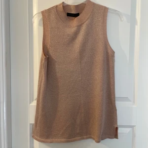 Glittrig nude ärmlös topp M&S - Säljer en nude-färgad ärmlös topp från M&S Collection. Toppen har en glittrig finish och ribbad rund halsringning. Perfekt för dig som gillar en enkel men ändå festlig look. Materialet är mjukt och stretchigt för en bekväm passform.