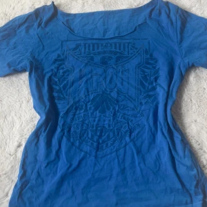 Blå Tapout t-shirt - blå tapout t shirt som blivit väl använd, men är i bra skick! har ett pytte litet hål som man ser på bild 2! klippt offshoulder själv! står ingen direkt storlek men gissar på S 🥰