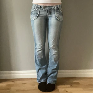 Ljusblå bootcut jeans från R&B - Säljer ett par ljusblå lågmidjade bootcut jeans från R&B med snygga detaljer på bakfickorna och dubbla knappar i midjan. Midjemåttet är ca 38 cm och innerbensmåttet ca 80cm! Okej skick förutom längst nere på ena byxbenet där de är lite slitna!😊