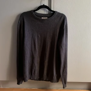Mörkgrå stickad tröja Jack & Jones - En stilren mörkgrå stickad tröja från Jack & Jones. Tröjan har rund halsringning, ribbade muddar och lång ärm. Tröjan är i mycket bra skick. Storlek L men sitter mer som M.