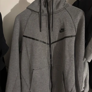 Grå Nike tech fleece  - Nike tech fleece, men den äldre modellen som inte sälja längre. Inte många som har just denna modell.  Storlek M kan passa folk med S, men då  lite baggy. Jackan har ett slitage, men annars funkar fint. Pris kan diskuteras. 