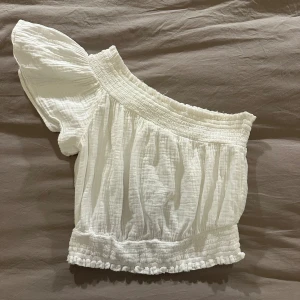 Vit offshoulder topp från Aerie - Superfin vit offshoulder topp från Aerie med en puffig ärm och smockdetaljer vid midjan och halsen. Toppen har en croppad passform som passar perfekt till varma dagar.