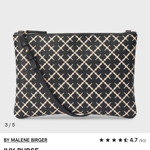 SÖKER - Snygg kuvertväska från By Malene Birger i svart och beige med grafiskt mönster. Väskan har justerbar rem och dragkedja upptill. Perfekt för att lyfta din outfit med en trendig touch.