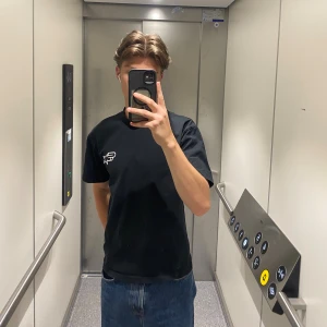 Svart SEAMS t-shirt med tryck - Svart t-shirt från SEAMS med vit logga på bröstet och stort tryck på ryggen. Klassisk rund hals och korta ärmar. Skön passform och tillverkad i mjuk bomull. Perfekt för dig som gillar streetwear och stilrena detaljer.