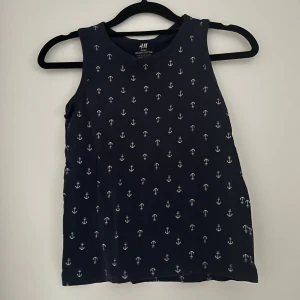 Marinblå linnetopp med ankare H&M - Säljer en marinblå linnetopp från H&M i ekologisk bomull. Toppen är ärmlös och har ett vitt ankarmönster över hela plagget. Perfekt för en chill sommardag eller strandhäng. Klassisk rund halsringning och mjukt material.