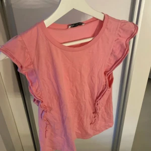 Rosa volangtopp från Zara - Supersöt rosa topp från Zara med volangdetaljer längs axlarna och sidorna. Toppen är ärmlös med rund halsringning och har en feminin, lekfull look. Perfekt för dig som gillar färg och vill sticka ut lite extra. Tillverkad i mjuk bomull.