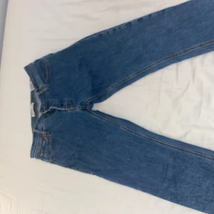 Blå jeans från Jack & Jones, 32/34 - Klassiska blå jeans från Jack & Jones i rak modell. Jeansen har fem fickor, snygga kontrastsömmar och en patch med logga bak i midjan. Tillverkade i bomull för en skön känsla och tidlös look.