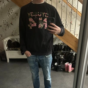 Svart Stussy sweatshirt med tryck - En skit fett vintage svart sweatshirt från Stussy i storlek medium. Tröjan har ett stort färgglatt Stussy-tryck på bröstet med inslag av rött och vitt rutmönster. Klassisk passform med rund hals och långa ärmar. Perfekt för en avslappnad streetwear-look.