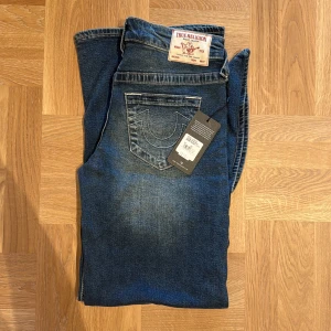 True Religion Bobbi Baggy Jeans blå - Säljer ett par True Religion Bobbi Baggy Jeans i mörkblå tvätt med coola kontrastsömmar och klassisk logga på bakfickan. Jeansen har en loose och baggy passform med raka, vida ben och är tillverkade i slitstarkt denim. Perfekta för en avslappnad streetstil.