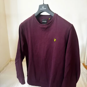 Vinröd sweatshirt från Lyle & Scott - Säljer en vinröd sweatshirt från Lyle & Scott med klassisk rund hals och gul logga broderad på bröstet. Tröjan är långärmad och har ribbade muddar vid ärmslut och nederkant. Perfekt för en chill och stilren look.  (storlek L)