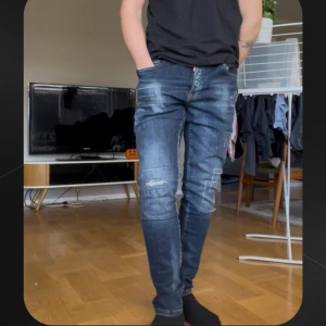 Dsquared2 Cool Guy Jean stl 33/Medium - Snygga blå jeans från DSQUARED2. Slim fit men inte supertight som Skateroch. Coola distressed slitningar samt tryckt logga på framsidan. Jeansen har detaljerade sömmar, patchade partier och klassisk femficksdesign. Perfekta för dig som gillar streetstyle och vill sticka ut. Passar 175-185cm. Storlek 33/medium. Alla lappar sitter kvar. Ej använda.