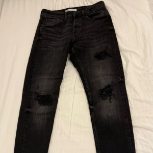 Säljer Grå/Svarta Zara Jeans! - Använd endast 3 gånger Storlek: EUR: 40 Svarta jeans med snygga slitningar på båda benen. 