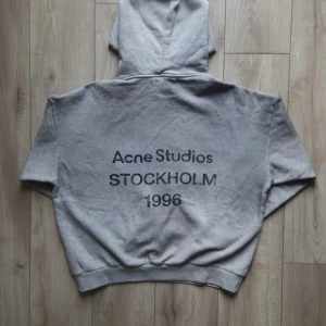 Grå hoodie Acne Studios S - Snygg grå hoodie från Acne Studios med tryck 'STOCKHOLM 1996' på ryggen. Oversized fit, mjuk insida och klassisk huva. Tillverkad i 100% bomull, perfekt för chill dagar. Diskret logga framtill och breda muddar vid ärmslut och midja.