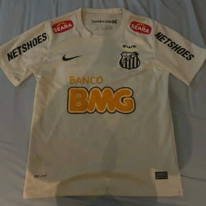 Santos FC Neymar Jr matchtröja  - Snygg vit Santos FC fotbollströja från Nike med Neymar Jr och nummer 11 på ryggen. Tröjan har korta ärmar, flera sponsorer tryckta på både fram- och baksidan samt klubbmärke på bröstet. Tillverkad i Dri-FIT material som andas och passar perfekt för träning.