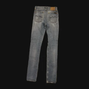 Blå jeans från Nudie Jeans - STORLEK (sitter 29.) LÄNGD: 34. Säljer ett par blå jeans från Nudie Jeans med slitningar och hål vid knäna för en riktigt avslappnad look. Klassisk femficksmodell med Nudie-logga på bakfickan och ljus tvätt. Perfekta för dig som gillar streetstyle och vill ha ett par jeans med attityd.