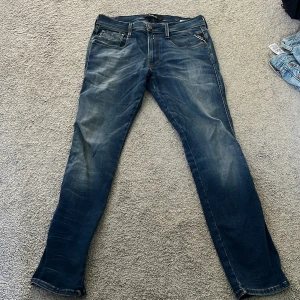 Replay Anbass hyperflex blå jeans herr - Säljer ett par Replay Anbass jeans i klassisk blå tvätt med snygga slitningar. Jeansen har fem fickor, normal passform och smalare ben. Tillverkade i stretchigt jeanstyg för extra komfort. Perfekta för dig som gillar en modern och stilren look.